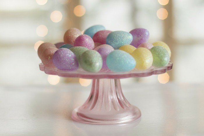 Huevos de Pascua con brillo en un soporte de pastel hecho de vidrio rosa