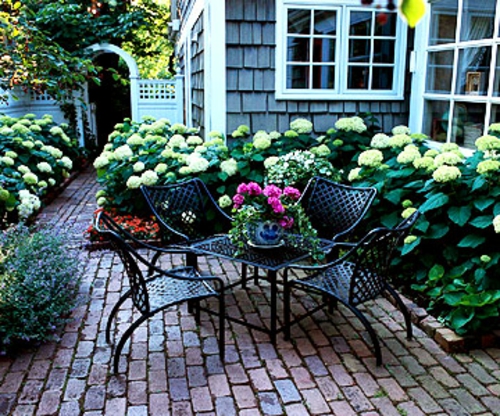 σκιερό καθιστικό στον κήπο μεταλλικές καρέκλες λουλούδια δομές
