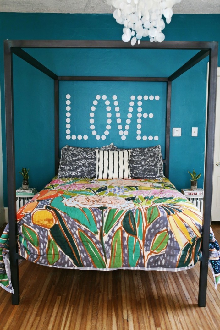 Miegamajame įrengtos spalvingos patalynės ir mėlynos sienos dažai