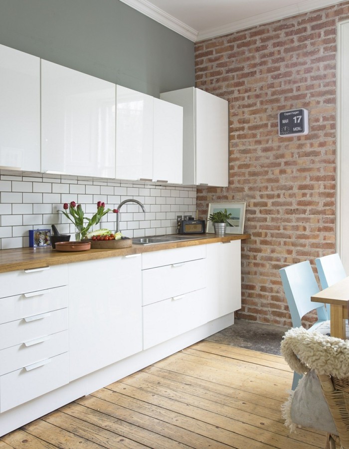 namų interjeras virtuvė plytų siena baltos spintelės durys ir medinės grindys
