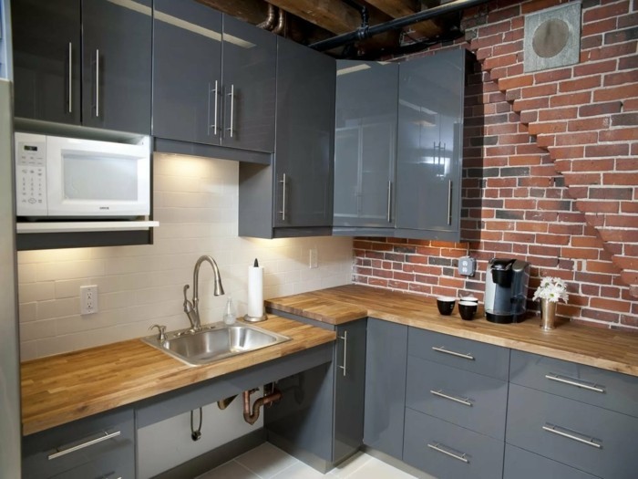 bakstenen muur en houten werkoppervlak van grijze keukenkasten